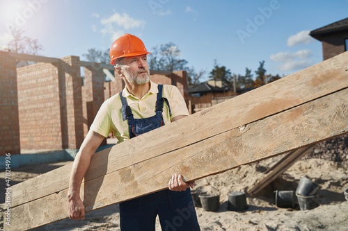 Construction worker carrying a wooden board on site