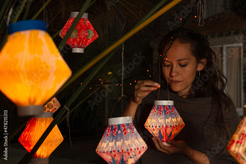Foto Hispanic woman holding a paper lantern while looking at it, under a plant decora