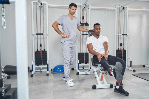 Calm focused man doing leg exercise supervised by physiatrist © Viacheslav Yakobchuk