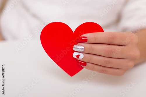 Beautiful female hand with romantic manicure nails, holding heart, valentine's day design