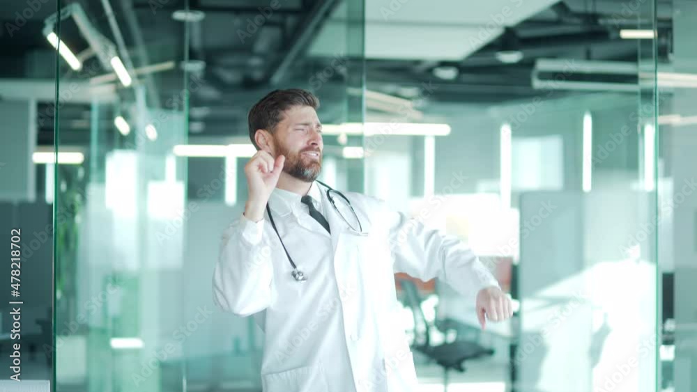 happy cheerful funny doctor dances with a stethoscope in a modern clinic or hospital. Male healer celebrates sings in office at work. health worker. handsome doc man in professional medical white coat happy cheerful funny doctor dances with a stethoscope in a modern clinic or hospital. Male healer celebrates sings in office at work. health worker. handsome doc man in professional medical white coat