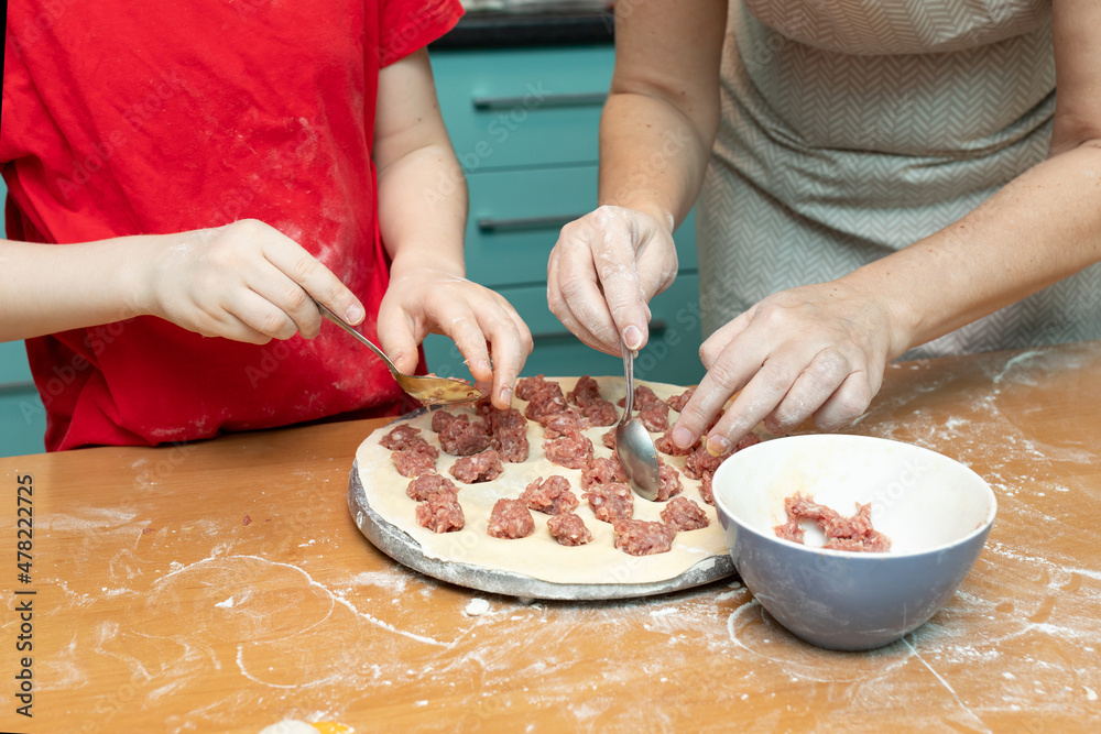 Process of cooking meat dumplings stuffed on the dough. Mother teaches her son cooking, working together in the kitchen Process of cooking meat dumplings stuffed on the dough. Mother teaches her son cooking, working together in the kitchen