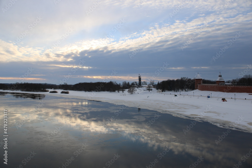 sunrise over the frozen river and old castle at the coast, clouds and sun reflected in water