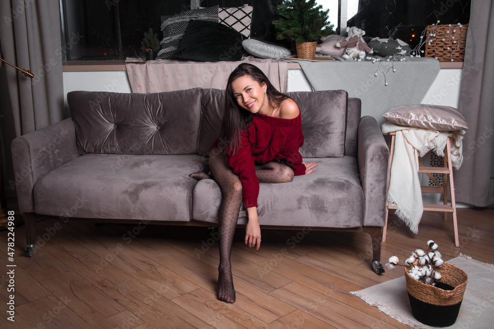 Obraz premium a girl in a red sweater on the sofa in a room with a Christmas decor.