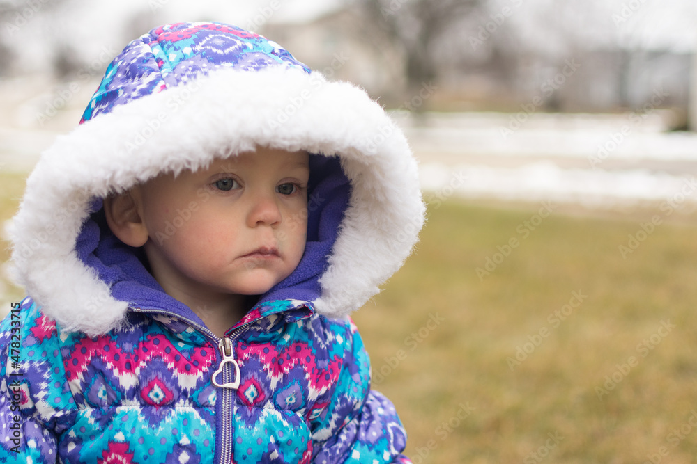18 month old baby girl in a colorful patterned snow suit and hood looks away from the camera with a serious expression; waiting for the snow to fall 18 month old baby girl in a colorful patterned snow suit and hood looks away from the camera with a serious expression; waiting for the snow to fall