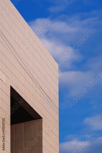Low angle view of apertures window on gray tile wall of office building against white clouds on blue sky in vertical frame 