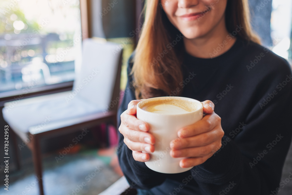 Closeup of a beautiful young woman holding and drinking hot coffee in cafe Closeup of a beautiful young woman holding and drinking hot coffee in cafe