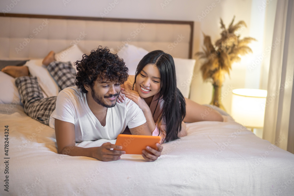 Woman and man lying on stomach with tablet Woman and man lying on stomach with tablet