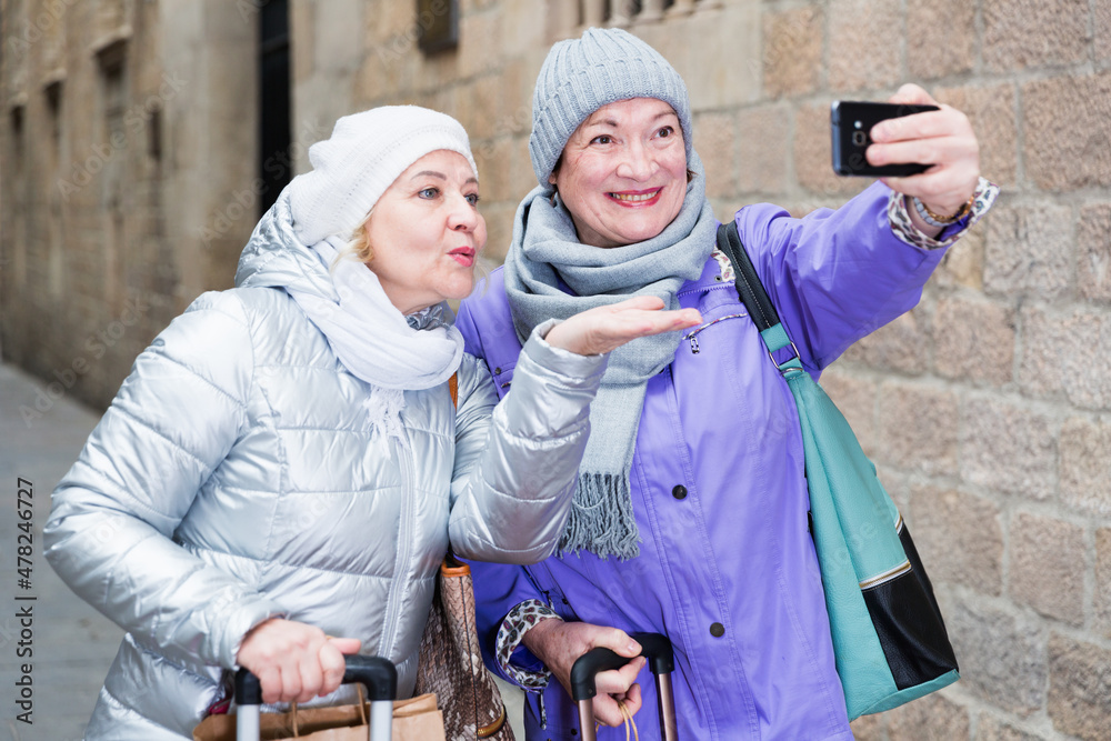 Senior woman with female friend traveling together and taking selfie with phone