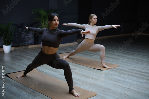 Two sportive women practicing doing yoga in the studio spreads their hands in different directions