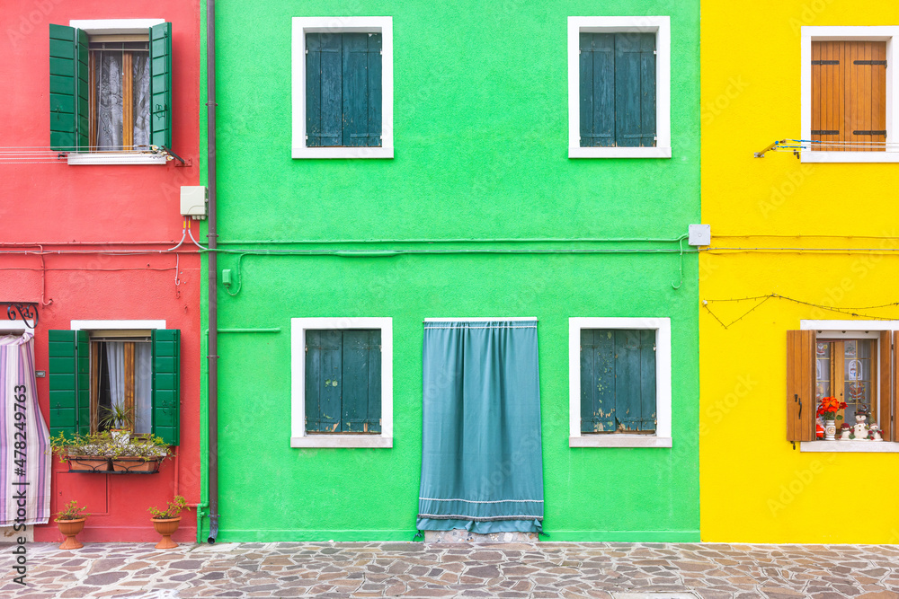 Naklejka premium Close up of a brightly colored two-story plaster facade with windows with flower pots and a door, the leftmost red, the center green, the rightmost is yellow