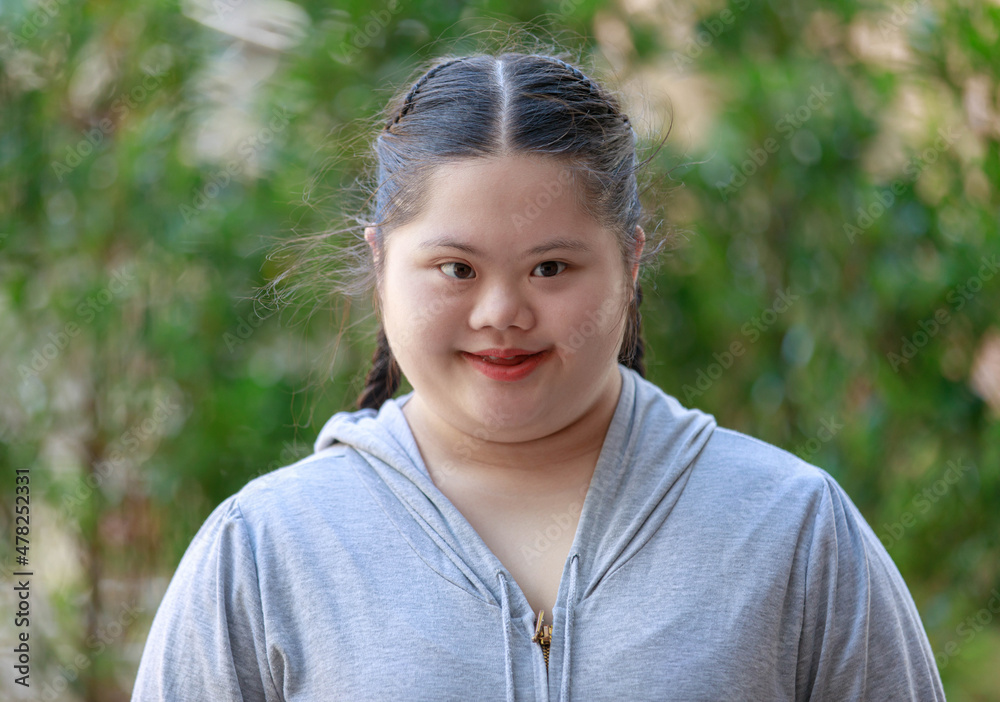 Portrait shot of Asian young chubby down syndrome autistic autism little cute schoolgirl with braid pigtail hairstyle model stand posing smiling look at camera in front blurred garden view background Portrait shot of Asian young chubby down syndrome autistic autism little cute schoolgirl with braid pigtail hairstyle model stand posing smiling look at camera in front blurred garden view background