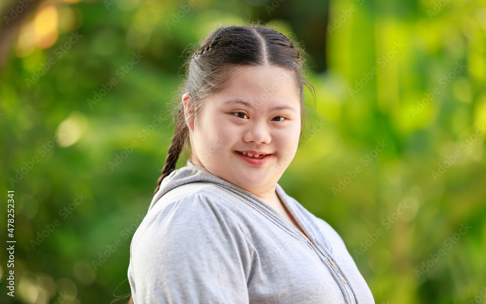 Portrait shot of Asian young chubby down syndrome autistic autism little cute schoolgirl with braid pigtail hairstyle model stand posing smiling look at camera in front blurred garden view background Portrait shot of Asian young chubby down syndrome autistic autism little cute schoolgirl with braid pigtail hairstyle model stand posing smiling look at camera in front blurred garden view background