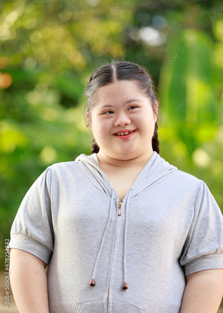 Portrait shot of Asian young chubby down syndrome autistic autism little cute schoolgirl with braid pigtail hairstyle model stand posing smiling look at camera in front blurred garden view background Portrait shot of Asian young chubby down syndrome autistic autism little cute schoolgirl with braid pigtail hairstyle model stand posing smiling look at camera in front blurred garden view background