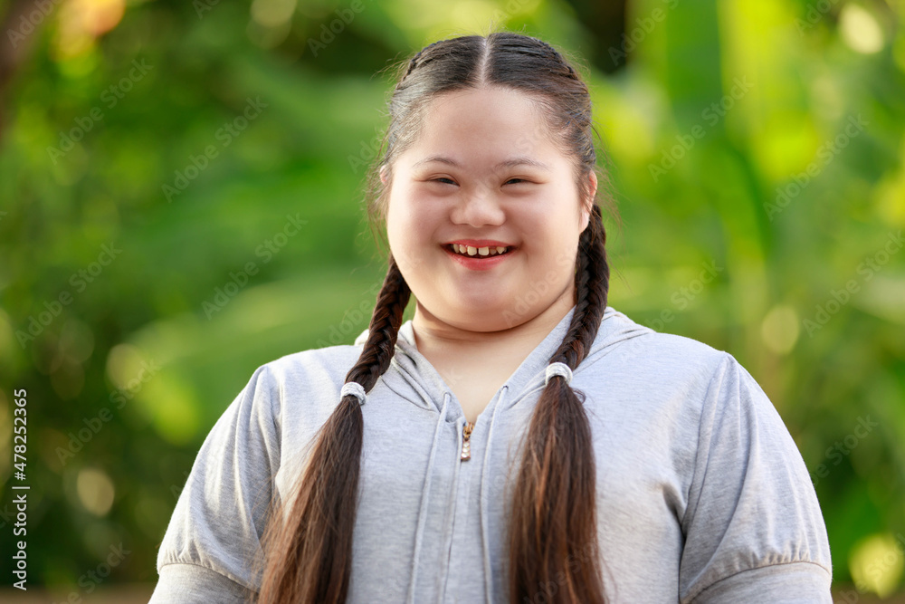 Portrait shot of Asian young chubby down syndrome autistic autism little cute schoolgirl with braid pigtail hairstyle model stand posing smiling look at camera in front blurred garden view background Portrait shot of Asian young chubby down syndrome autistic autism little cute schoolgirl with braid pigtail hairstyle model stand posing smiling look at camera in front blurred garden view background