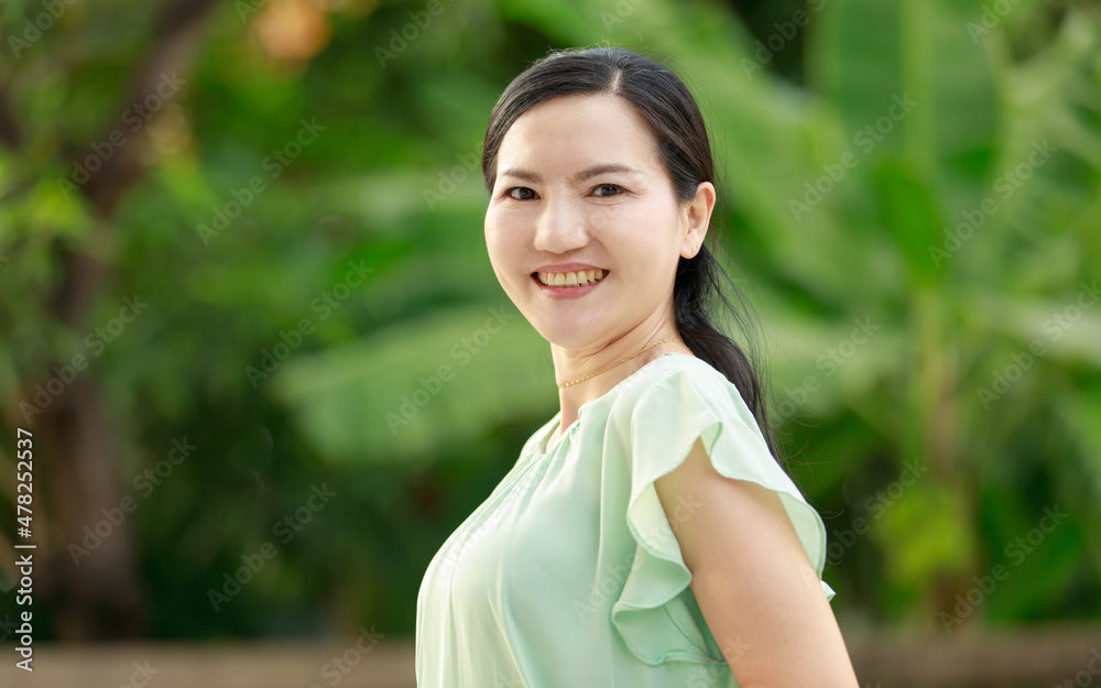 Portrait shot of Asian young mature beautiful happy pretty long ponytail hairstyle female model in green casual outfit standing posing smiling look at camera in front blurred garden view background Portrait shot of Asian young mature beautiful happy pretty long ponytail hairstyle female model in green casual outfit standing posing smiling look at camera in front blurred garden view background