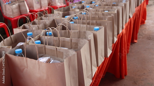 A water bottle and snacks are placed in a brown paper bag on a red table.