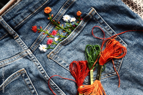 Creative DIY project, hand embroidery at home on jeans, creative hobby, clothes recycle, floral embroidery design, colorful threads, embroidery needle photo