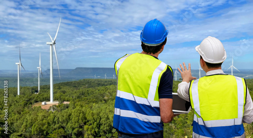 Windmill engineer man and worker standing and planing renewable energy technology or alternative ecology project for future. Electrician engineer looking and checking wind turbines site with computer