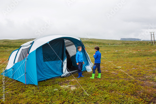 Happy children, standing in front of a tent on a lawn in arctic circle