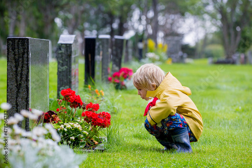Sad little child, blond boy, standing in the rain on cemetery, sad person, mourning photo