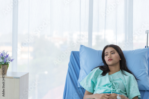 Portrait of young Asian female patient with hospital clothes feels sad, unhappy and bad, is thinking about her disease and her treatment after surgery on hospital bed in hospital.