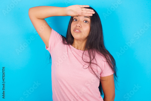 Young hispanic girl wearing pink T-shirt over blue background wiping forehead with hand making phew gesture, expressing relief feels happy that he prevented huge disaster. It was close enough photo