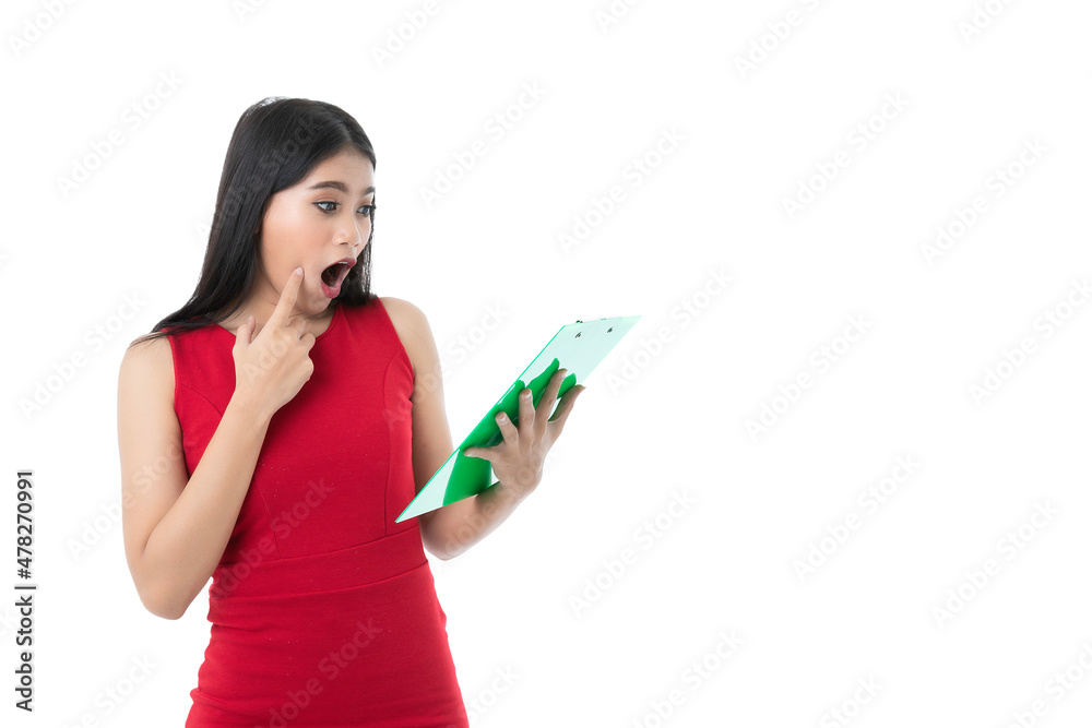 Happy beautiful young Asian business woman in casual business red dress is shocking, pointing on cheek, looking green clipboard, feels surprised, amazed, isolated white background. Clipping path Happy beautiful young Asian business woman in casual business red dress is shocking, pointing on cheek, looking green clipboard, feels surprised, amazed, isolated white background. Clipping path