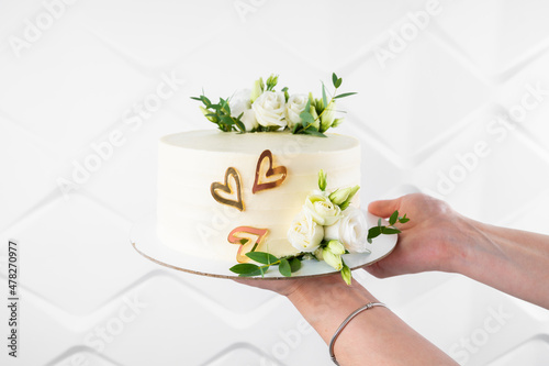 Pastry chef holding tasty wedding cake with floral decoration on white background, close up