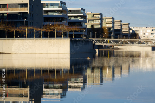 Apartment buildings at border of pond at public park with bridge in the background on a sunny winter day. Photo taken December 31st, 2021, Zurich, Switzerland.