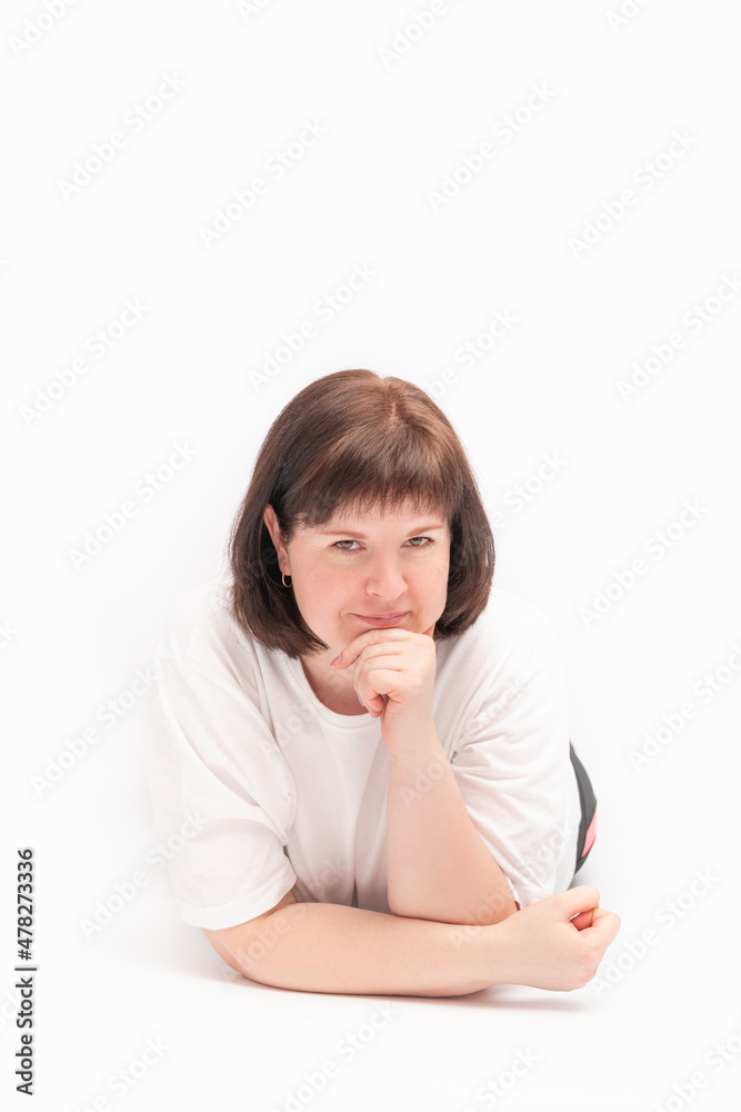 Portrait of charming cute young round-faced woman with dark hair lies with fist on her chin and looks at camera on white background. Vertical frame. Portrait of charming cute young round-faced woman with dark hair lies with fist on her chin and looks at camera on white background. Vertical frame.