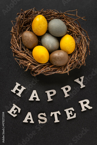 Easter eggs in birds nest and the inscription Happy easter on dark background.