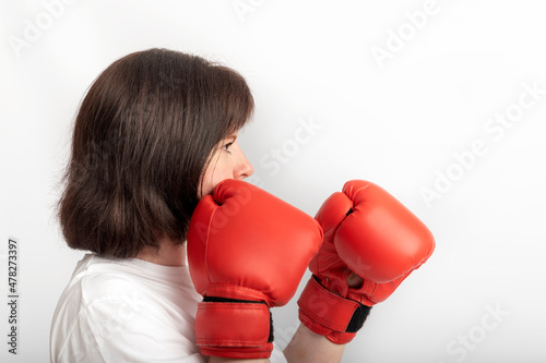 Portrait of young female boxer in red gloves on white background. Struggle for womens rights, feminism. Side view photo