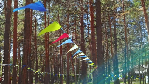 Happy hollidays triangle flags on string. Celebrate birthday decoration blowing on wind. Pine forest background. Colorful symbolic. Carnival fiesta design. Slow video photo