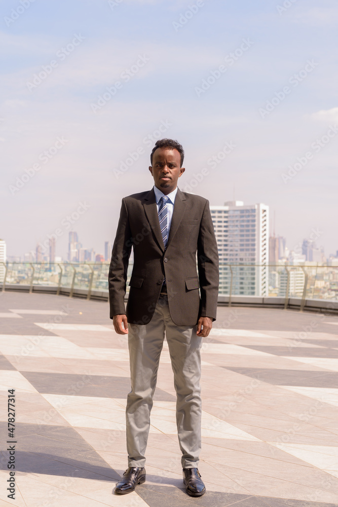Full length portrait of African businessman wearing suit and tie outdoors in city while standing Full length portrait of African businessman wearing suit and tie outdoors in city while standing