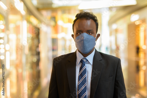 Portrait of African businessman wearing suit and face mask while social distancing