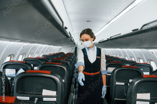 In protective gloves and mask. Young stewardess on the work in the passanger airplane