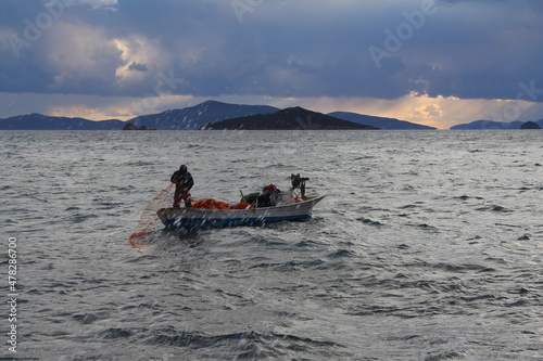 A fisherman who tries to catch fish in a tiny small boat in the Aegean Sea among the waves in a rainy day.