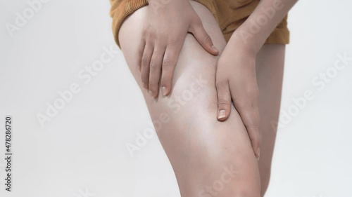 White woman kneads her thigh with her hands, closeup, studio. Woman's hands are kneading leg that hurts. Concept of varicose veins photo