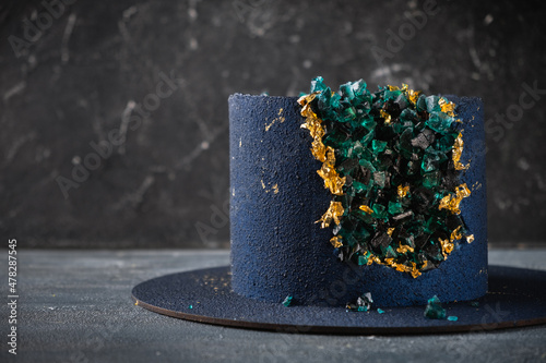Luxury mousse cake covered with blue velvet coating and decorated with golden petals on the dark background. Shallow depth of field