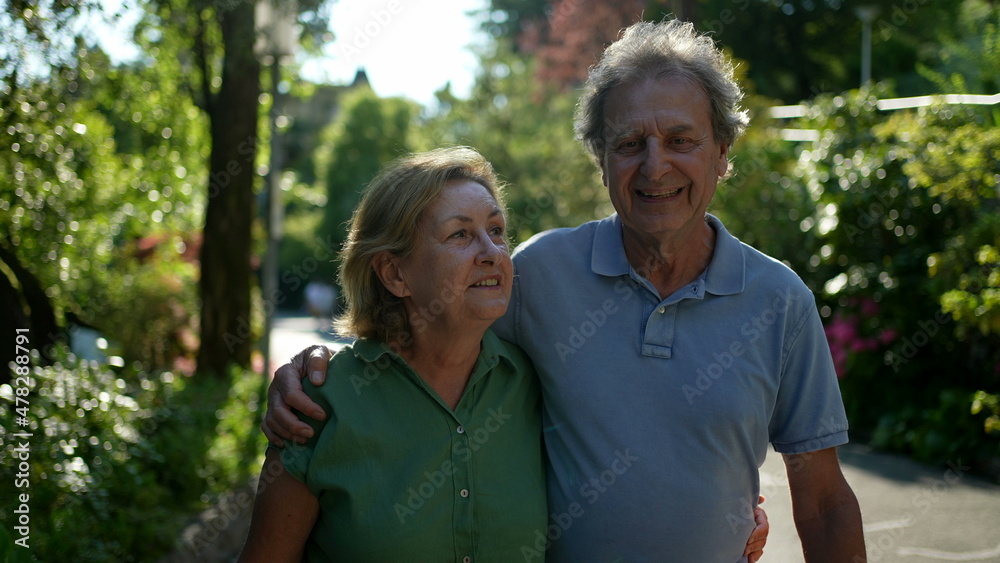 Two happy older people walking outside smiling, senior couple together in outdoor nature walk