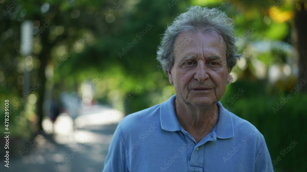 Smiling senior man walking outside in green path, one happy older person