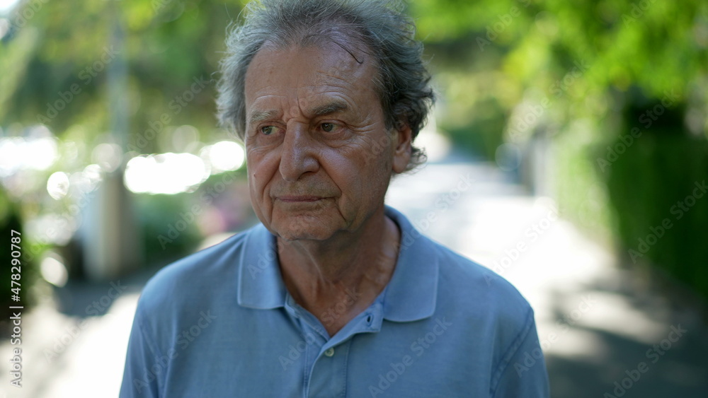 Pensive senior man walking outside in city green nature path Pensive senior man walking outside in city green nature path