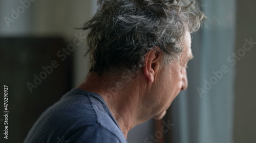 Pensive senior man standing by window looking outside. Thoughtful old person