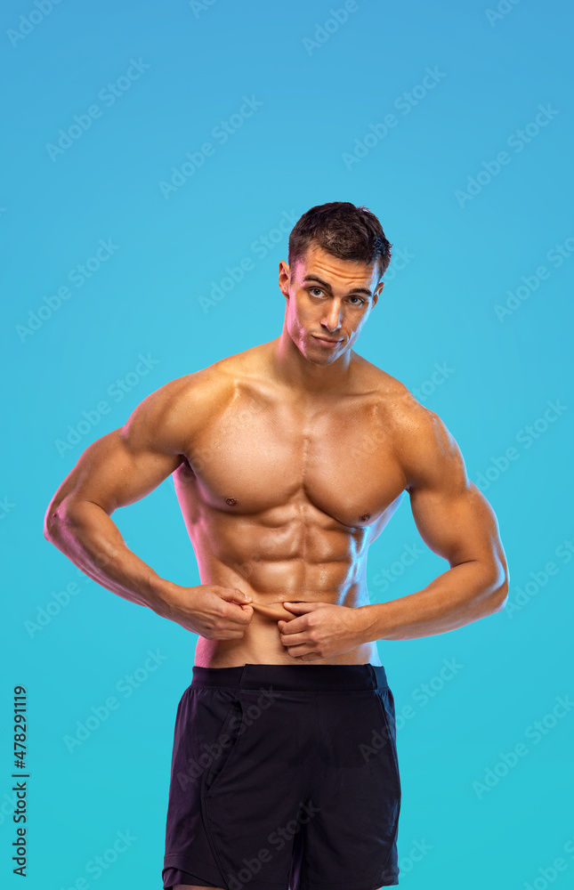 Happy man athlete shows how little subcutaneous fat is in his body. Sportsmen isolated on color background. Fitness motivation.