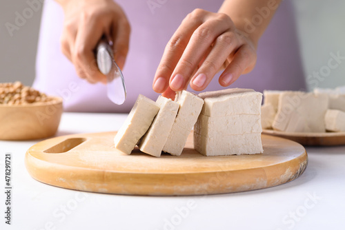 Hand holding knife and cutting organic tofu on wooden board prepare for cooking, Vegan food ingredients in Asian cuisine, plant based