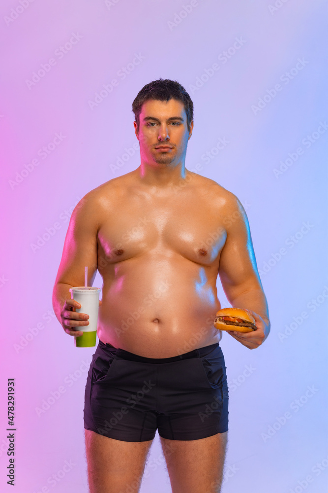 Fat man with burger and soda. Not sporty men drinking and eating hamburger isolated on pink background.