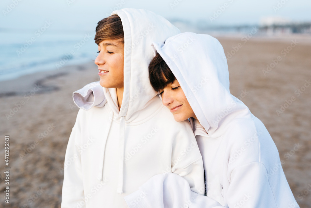 Portrait of two preteen brothers wearing white hooded sweater on the beach, on winter