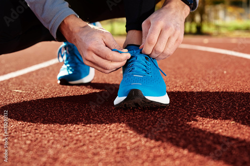 Male runner in blue sneakers get ready for run at stadium track, close up. Male hands tying on sport sneakers for jogging. Fitness and healthy lifestyle concept