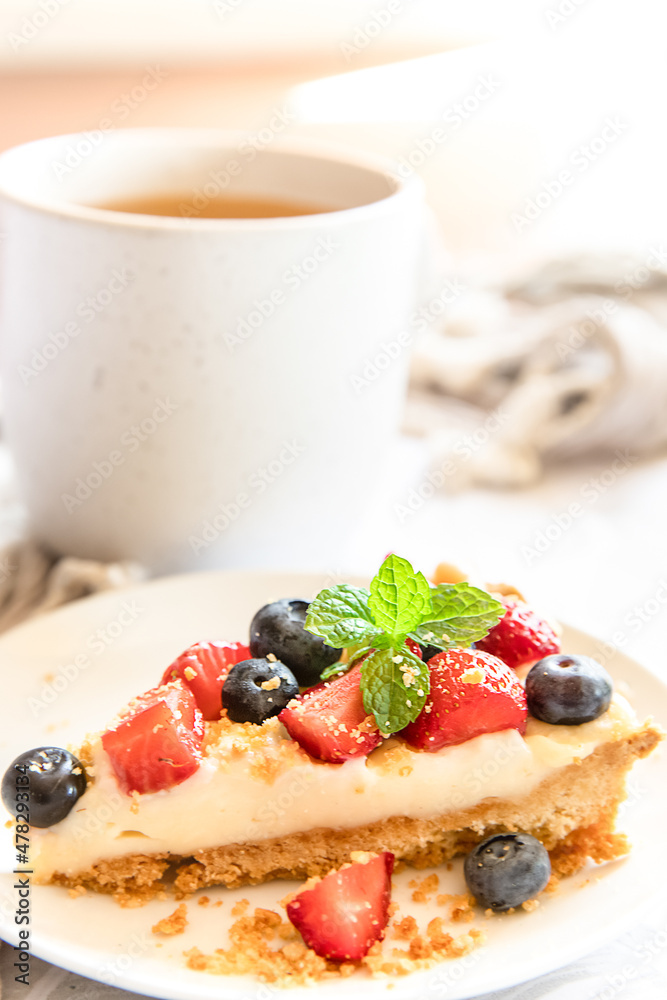 piece of strawberry and blueberry cheescake on plate and cup of tea served for breakfast at home, hotel or cafe. Dessert meal, sweet food . High quality photo